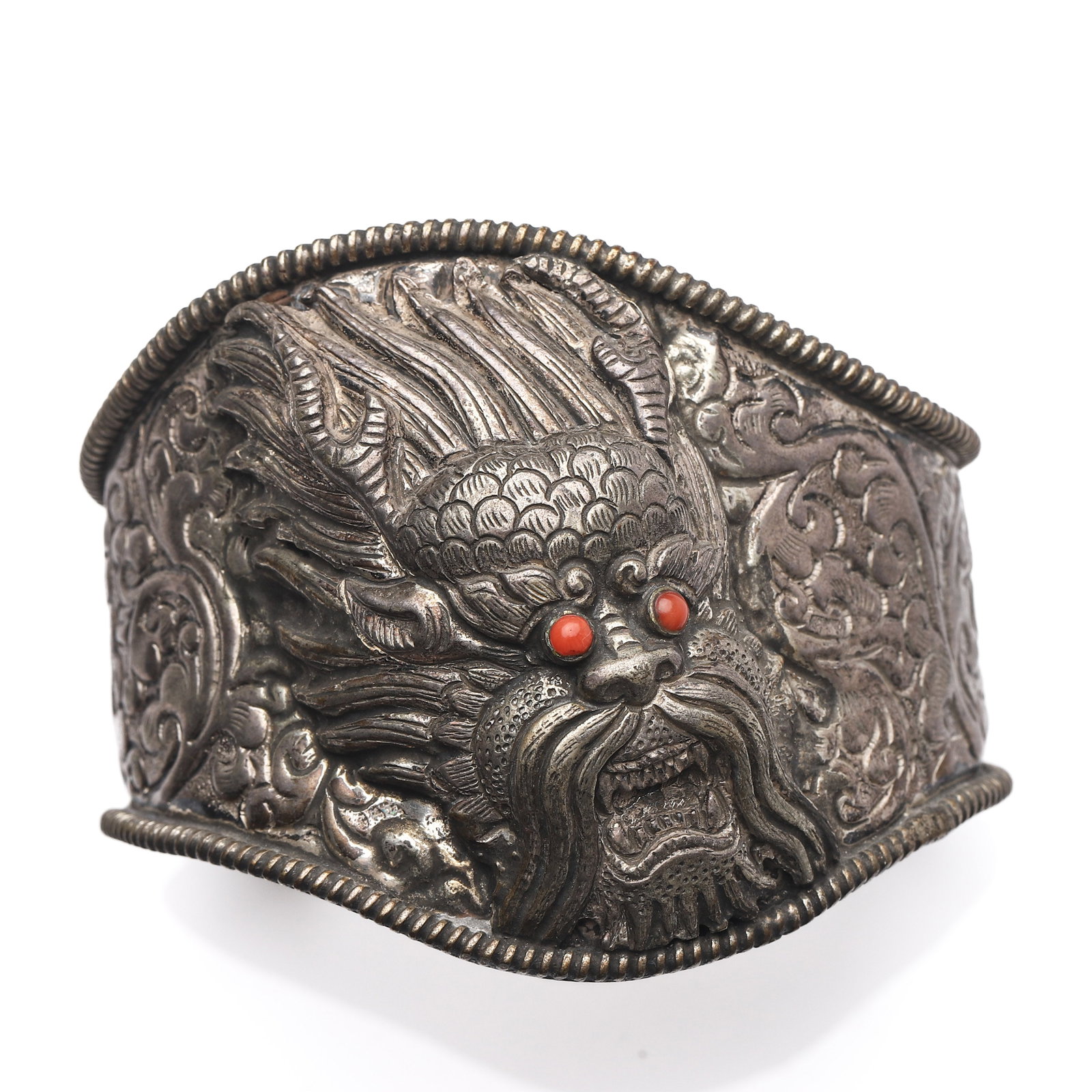 A SILVER DRAGON BRACELET: Dimensions Length: 3 1/8 in (8 cm)Weight: 107 g Description The wide cuff bracelet is richly repoussé and chased with scrolling motifs and centered with a dramatic dragon mask in high relief, its fie