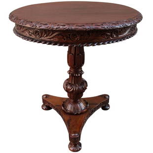 19th C British Colonial Rosewood Occasional Table: A British Colonial Regency solid rosewood table made in India, circa 1830, featuring an elaborately carved apron and tripod pedestal base with bun feet.