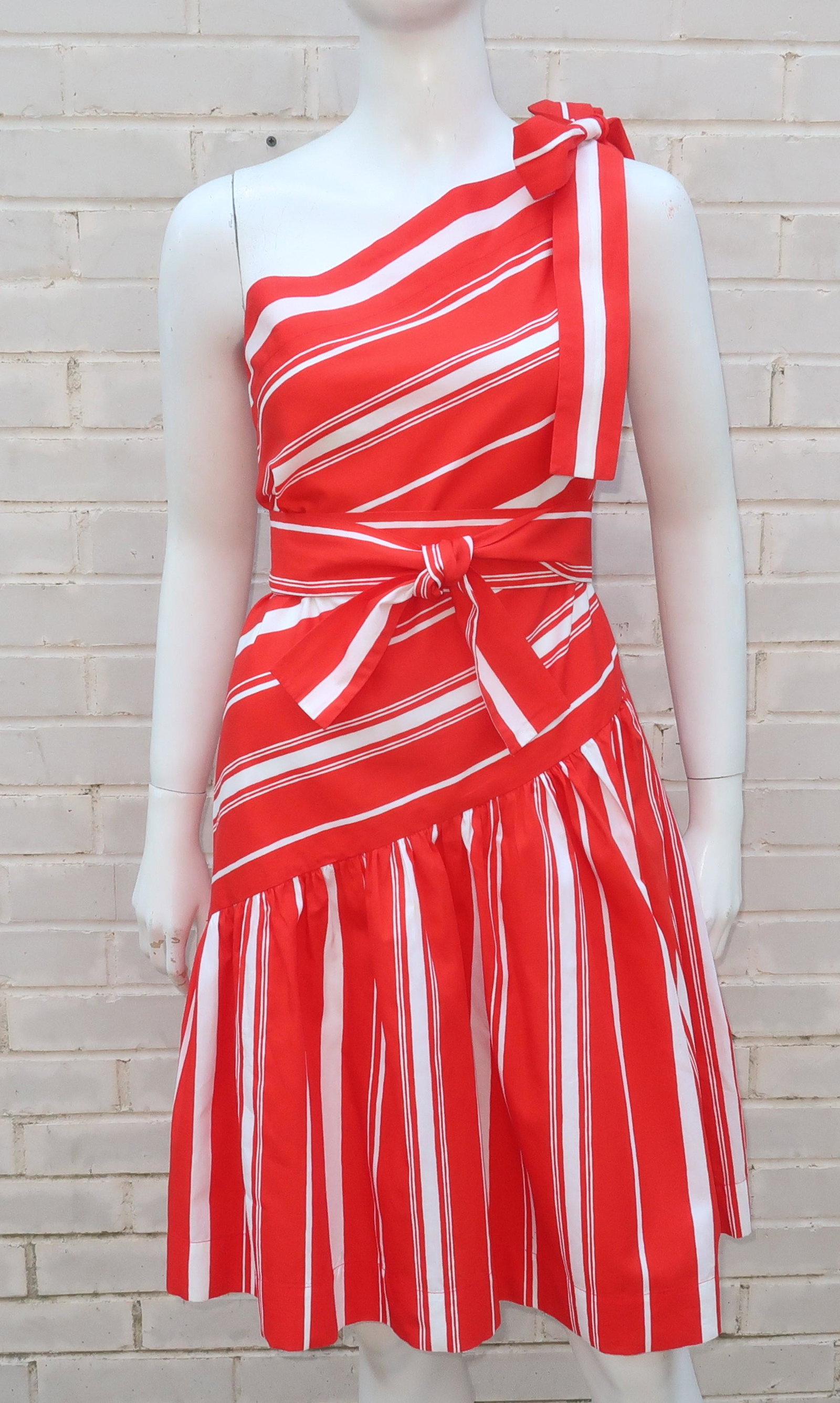 Yves Saint Laurent 1970's Striped Sun Dress: 1970's Yves Saint Laurent red and white candy stripe cotton sundress. The pullover construction features an asymmetrical one shoulder drop waist bodice with a gathered skirt all accented by a tie at t