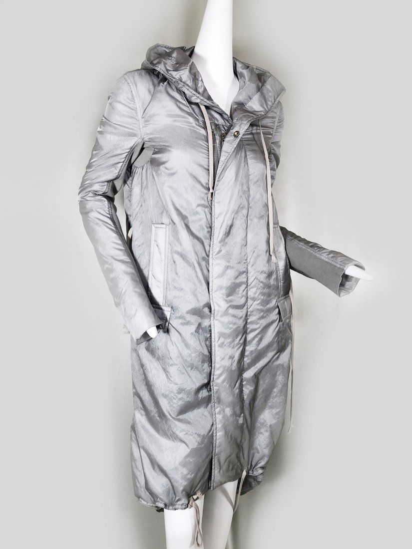 Rick Owens Silver Nylon Hooded Raincoat with Tails: A rare and sporty silver satin military-inspired mid-calf length hooded raincoat with zip down front and snap flap. Arms are fitted with an elasticized panel from cuff to underarm. Drawstring bottom h