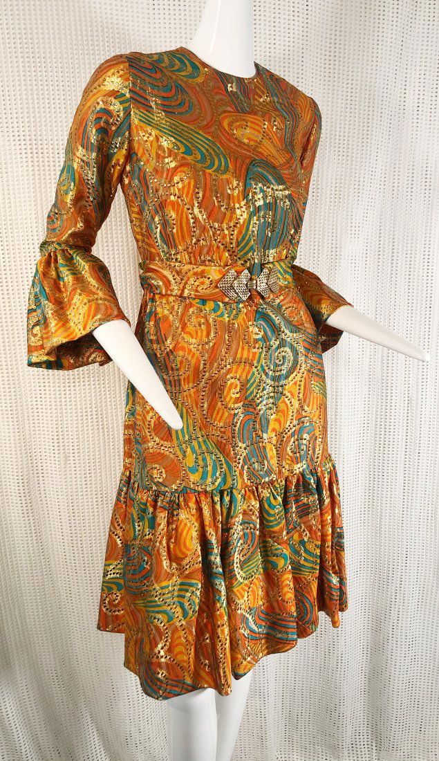 1960s Roger Milot Lame Paisley Cocktail Dress in Copper: A 1960s Roger Milot for Fred Perlberg lame paisley cocktail dress in copper, gold and green: Deep ruffled cuffs and hem. Rounded neckline and belt buckle detail.