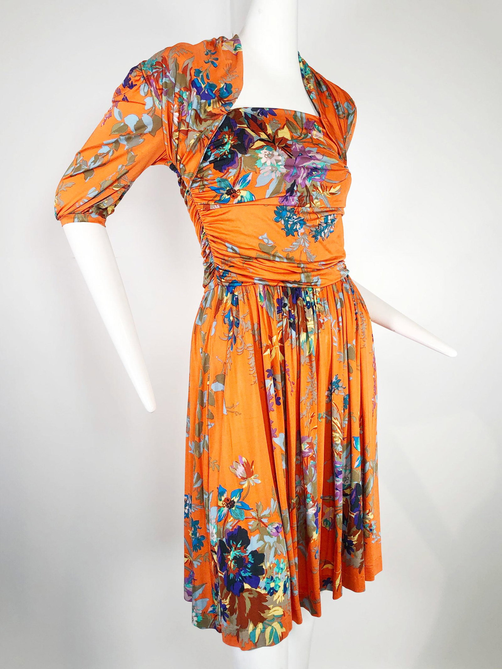 Etro Orange Jersey Floral Patterned Dress: Etro for Saks Fifth Avenue orange with polychrome floral pattern dress. 1940s inspired. Bodice has faux shrug look, gathered sides, and elbow length sleeves. Rayon stretch knit with small amount of ny