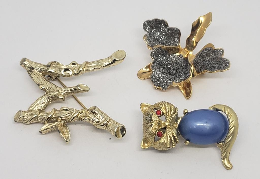 3-VINTAGE GOLD TONED BROOCHES: (1)LILLY WITH: GLITTER ACCENTS (1)SARAH COVENTRY "M" INITIAL (1)CAT WITH BLUE LUCITE BELLY AND RED RHINESTONE EYES