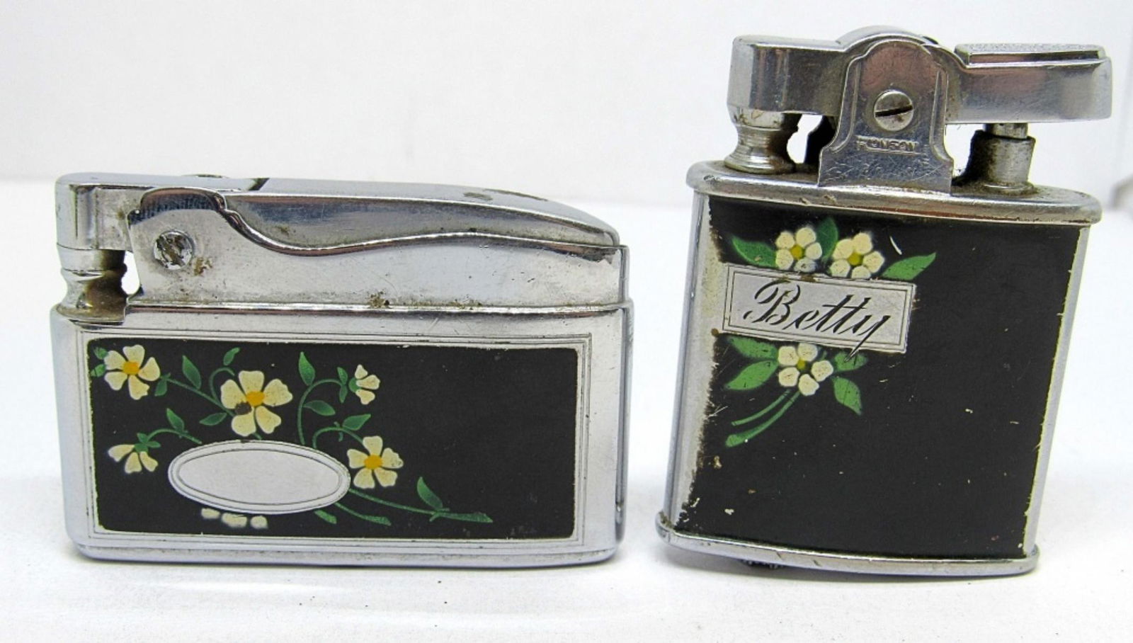 MATCHING FLORAL RONSON LIGHTERS: A PAIR OF BLACK FLORAL LIGHTERS. ONE IS A VINTAGE RONSON "PRINCESS" LIGHTER, AND THE OTHER IS RONSON "VENUS" LIGHTER. UNTESTED