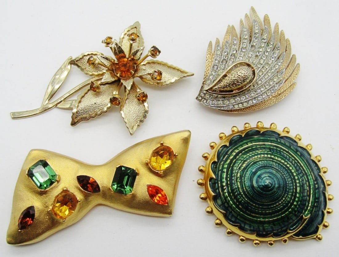 (4) LARGE GOLD TONE BROOCHES: ALL BETWEEN 2 1/2 AND 3IN LONG, GOLD TONE, 1 FLOWER WITH YELLOW STONES IN THE PETALS, 1 A BOW WITH DIFFERENT GEMS AND COLORS, 1 CLEAR STONE AND GOLD TONE WING, 1 GREEN INLAY SEASHELL