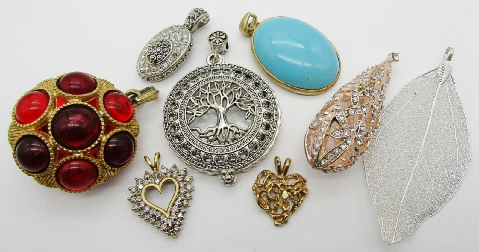 (8) WOMENS PENDANTS LOT: ALL ARE BETWEEN 1IN TO AND 3IN LONG, ROSE GOLD TONE TEARDROP WITH CLEAR STONES, 1 GOLD TONE CIRCLE WITH RED STONES ALL AROUND, 2 HEARTS, 1 CLEAR STONE OVAL, A SILVER TONE LEAF, 1 GOLD TONE SLEEPING BE