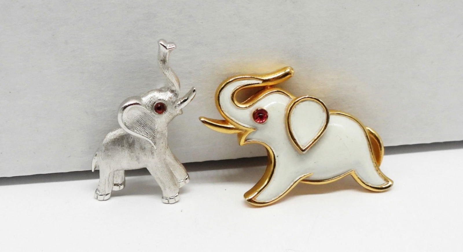 2 TRIFARI Elephant Pins: Two TRIFARI Elephant Pins. One is Brushed Silver Tone with a red gemstone eye. The Other is Gold Tone with White Enamel and a Red Gemstone Eye.