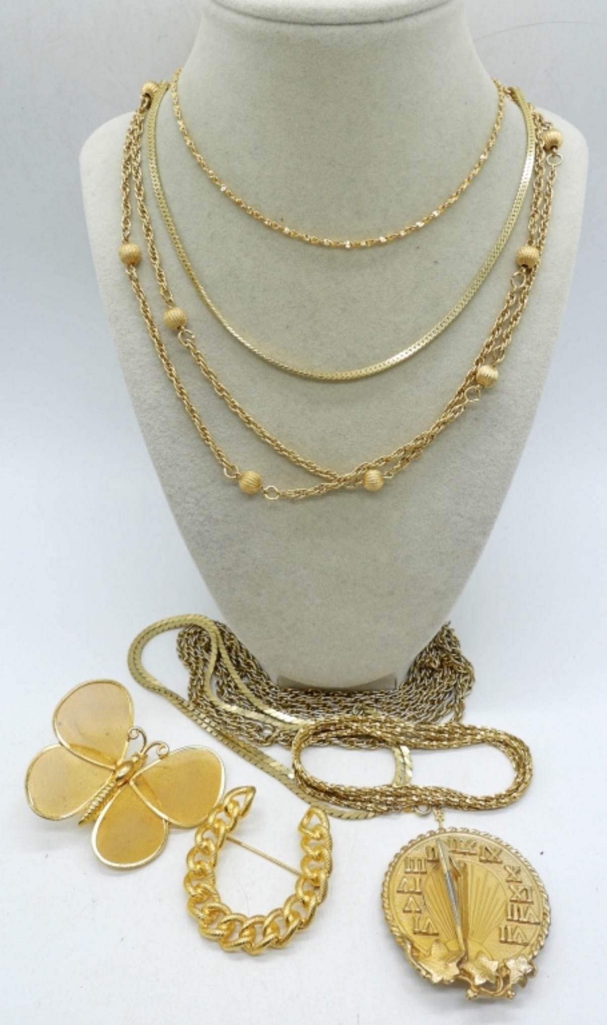 GOLD TONE CHAINS & BROOCHES: 6 GOLD TONE CHAIN NECKLACES. ONE IS TRIFARI. 18"-52". NAPIER GOLDEN TIME SUNDIAL BROOCH & TWO OTHER GOLD TONE BROOCHES. 2-3".
