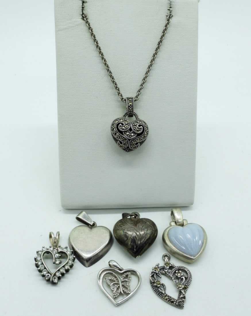 7 Sterling Heart Shaped Pendants & Chains: Seven sterling heart shaped pendants, all around 1" long. One sterling chain, 16" long. (16 dwt)