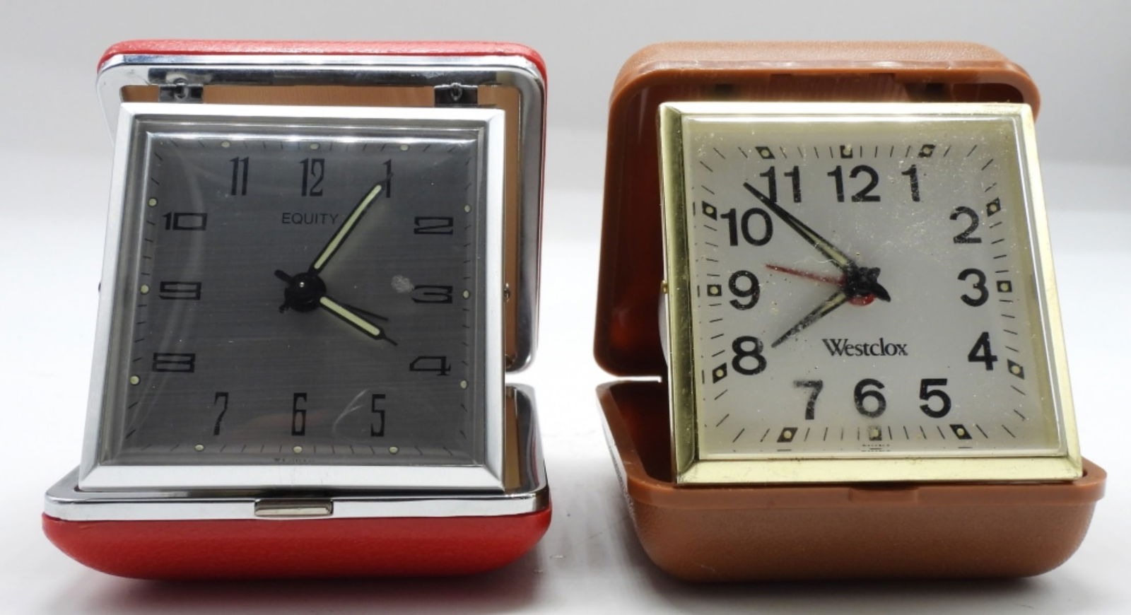 (2) Wind-Up Travel Alarm Clocks: Both clocks come in a hard travel case. On red, one brown. For parts. Watches are not verified, authenticated, or tested in running condition unless specified.
