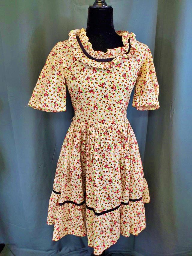 Vintage 1970s/80s Country Floral Dress: Vintage 1970s/80s Country Floral Dress with a ruffled neckline and black velvet ribbon. Measurements while laying flat are bust 16", waist 14", and 21" long from waist to hem. A small tear at the side