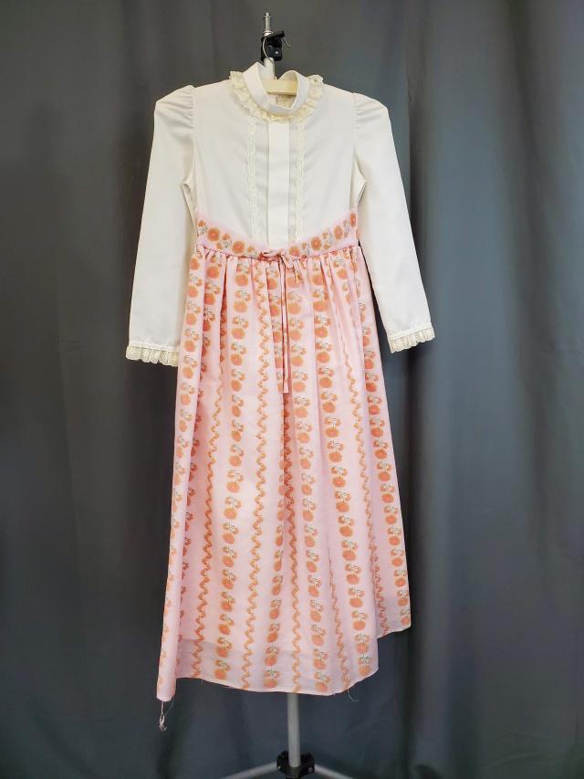 Vintage Girls Long Dress c1970s: Vintage c1970s girls dress with white top, long sleeves and lace on collar and cuffs, and a pink floral skirt with bow at the waist. Back zipper. Measurements while laying flat 14" bust, 12" waist, an