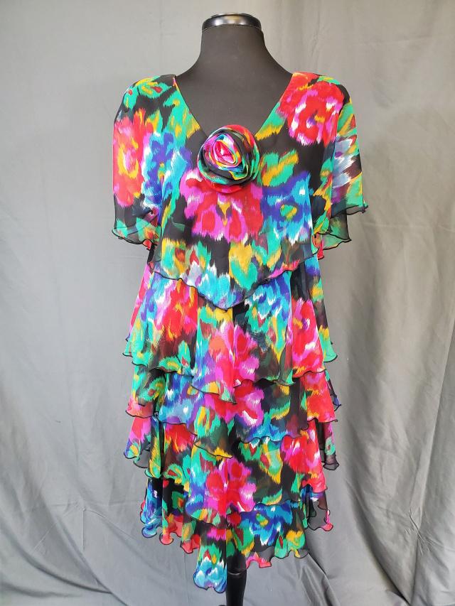 Vintage Ann Hobbs Cattiva Floral Ruffled Dress: Vintage Ann Hobbs Cattiva Floral Ruffled Dress with bright colors and a flower embellishment at the V neck. Has shoulder pads. Measurements while laying flat 18" bust, 16" waist, and 22" long from wai