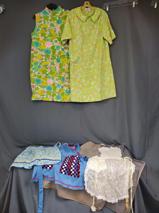 Group of Vintage Aprons: Includes two full aprons made of ticking, a green floral polyester house dress by Sears, a retro sleeveless housedress by Spiegel, a red white and blue full apron with rick rack, a blue print cotton h