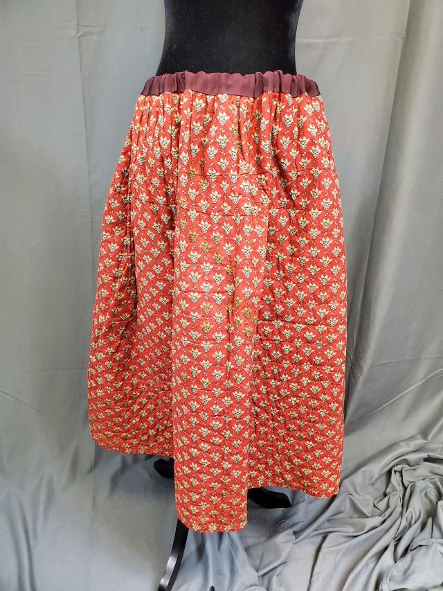 Antique Hand Quilted Petticoat - Large: Antique 1860-1870s hand quilt petticoat with a madder print and double green print lining. Cotton batting and hand quilted. It measures 22" along the waist when laying flat, but has a drawstring to ma