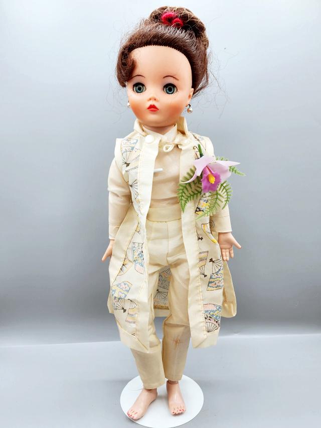 Vintage Uneeda Dollykins 19 inch Doll: Vintage Uneeda Dollykins 19 inch Doll, circa 1950s, dressed in ivory pants, top and a Japanese style long vest. Her hair is still in the original net. She is missing her shoes. Includes a stand. We do