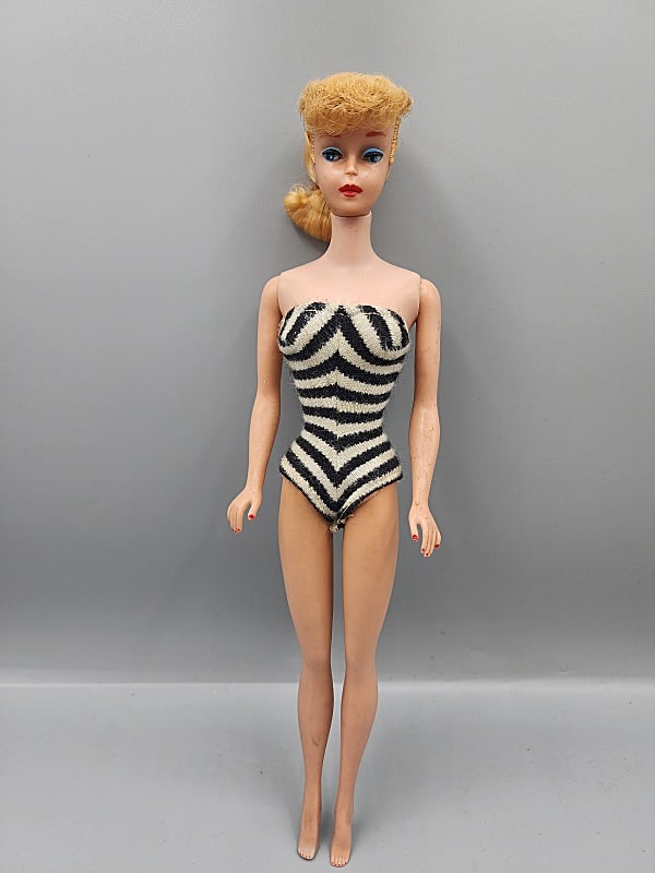 Vintage Barbie - Ponytail Blonde: Vintage Barbie-Ponytail Blonde, S/L. She is wearing a black and white striped bathing suit. She does have small marks on her legs and arms and green marks by her ears and minor tackiness on her arms a