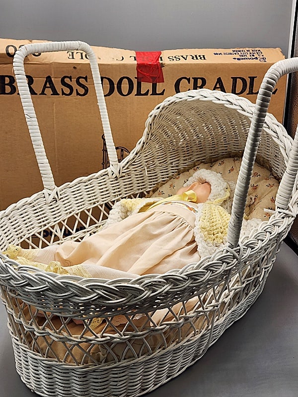 2 Cradles-Brass, Wicker with Doll: 2 Cradles-Brass, Wicker with Doll. Includes a brass doll cradle by Powell, still in original box, believed to be complete with instructions. Along with a white wicker bassinette measuring 19x13x12". I