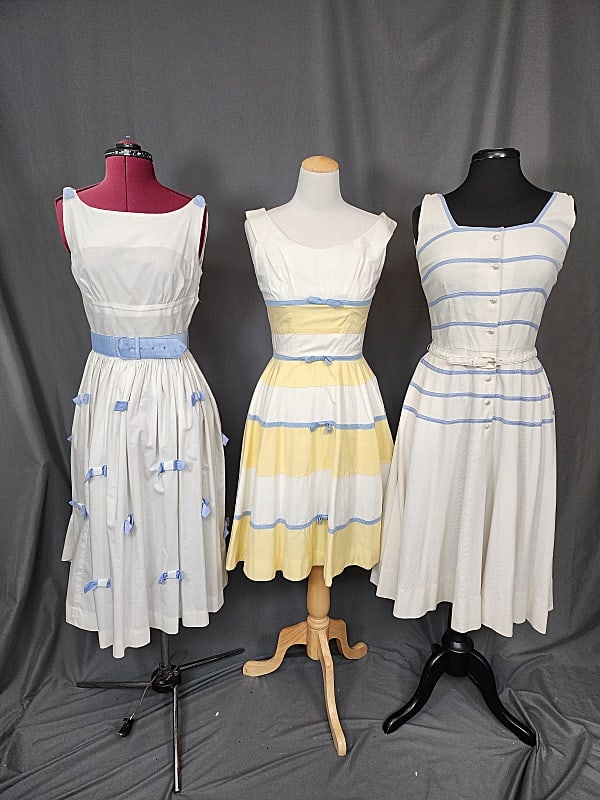 3 Vintage c1960s Sleeveless Dresses: 3 Vintage c1960s Sleeveless Dresses. Includes a white textured fabric A-line dress with blue horizontal trim stripes and pearlized buttons, belt, tag by Serbin, measures laying flat: 17" bust, 13" wai