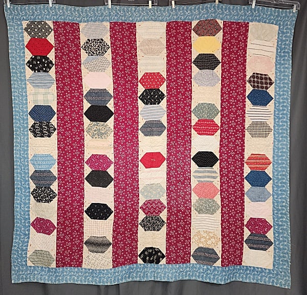 Antique 1904 Elongated Hexagon Quilt: Antique 1904 Elongated Hexagon Quilt measuring 76x75". Comprised of 5 vertical bars containing 15 elongated hexagons with 7" claret print bars. There is a 4" cadet blue border. It is hand and machine 
