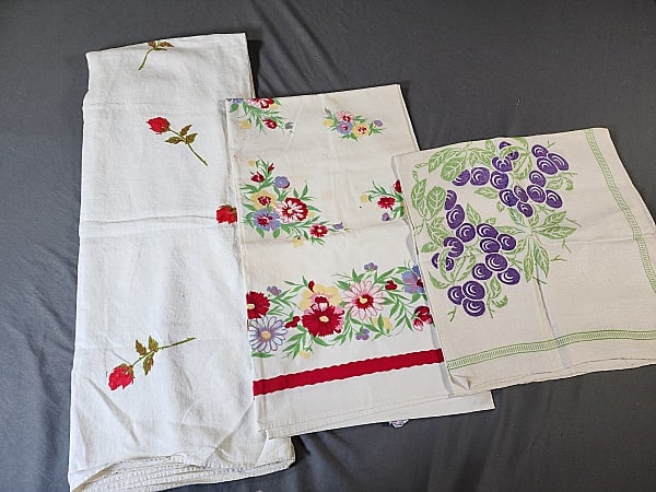 3 Vintage Printed Tablecloths: Group of 3 vintage printed tablecloths. Includes small linen cloth with grapes measuring 33" x 34", has small spots. Cotton floral tablecloth by Wilendur, measures 48" x 53", several dark spots & a sm