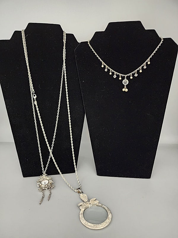 3 Silver Tone Necklaces-1928 and More: Group of 3 Silver Tone Necklaces-1928 and More. The group includes 1 silver tone cuckoo clock watch necklace/brooch featuring wonderful detailing and marcasite accents. As well as a white clock face w