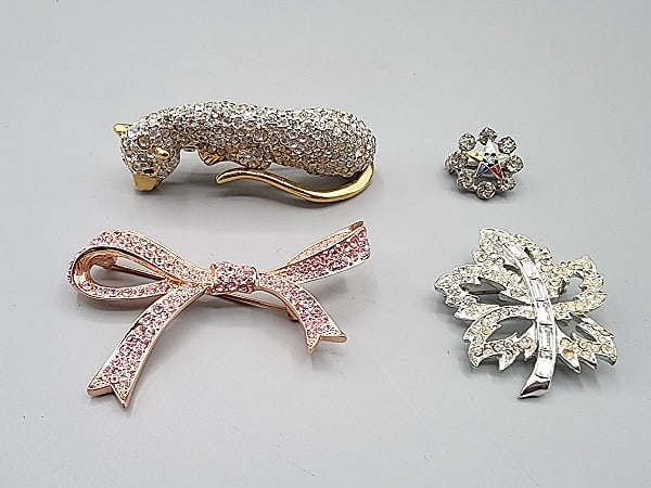 Group of 4 Brooches-Kenneth Jay Lane and More: Group of 4 Brooches-Kenneth Jay Lane and More. The group includes 1 rose gold tone bow brooch studded with pink rhinestones by Kenneth Jay Lane measuring 2.5'' wide by 1 3/4'' long. In good condition.