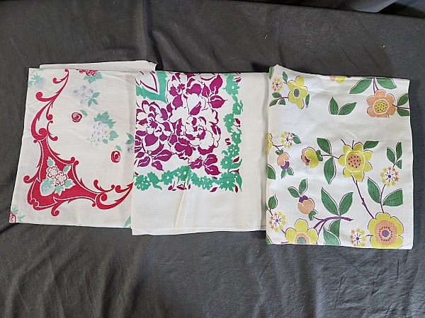 3 Vintage Printed Tablecloths-Fruit and Flowers: Group includes off-white cotton with yellow, orange, and green flowers, measures 47"x54", has several large spots. White rayon blend with claret and green flowers and leaves, measures 51"x47", some fa