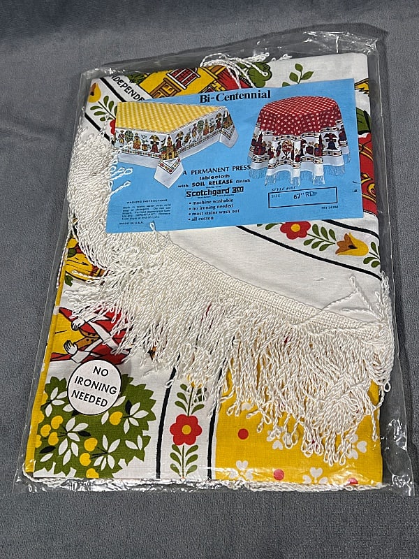 Vintage Printed Round Tablecloth - NIP Colonial: Vintage Printed Round Tablecloth - NIP Colonial. New in original package, 67" round Bi-Centennial pattern in yellow, orange and green with white fringe. In new, never used condition. From the estate o