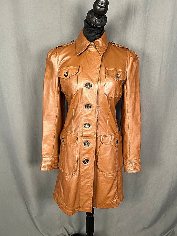 Ladies Leather Trench Coat: Ladies Leather Trench Coat. The lot includes a 1970s inspired ladies brown sheep leather trench coat featuring a fold over collar, zip and button closures, an adjustable back strap, and a quilted poly