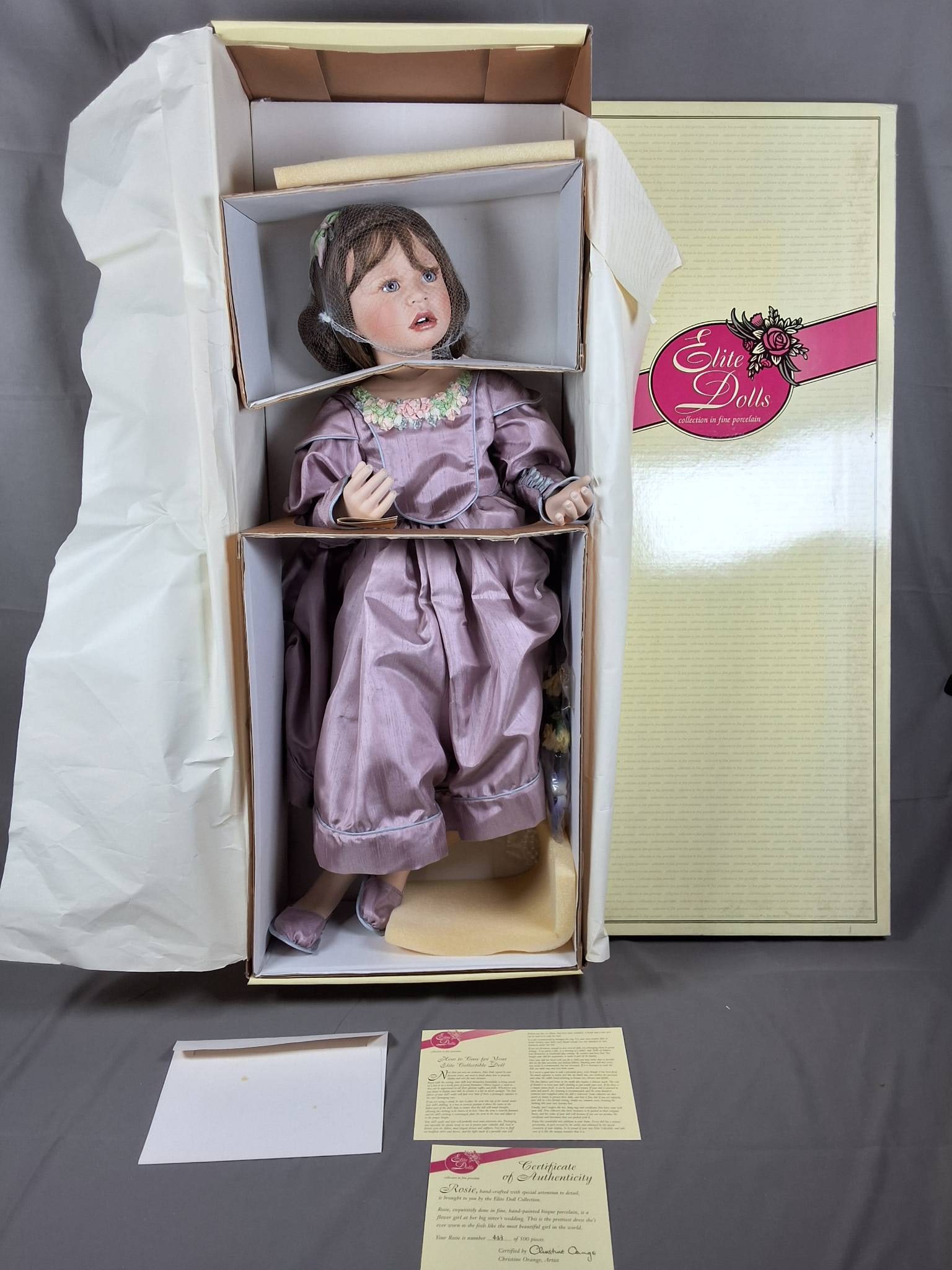 Elite Porcelain Doll Rosie: Elite porcelain doll named Rosie, limited edition numbered 433 of 500. Measures 31 inches tall. The doll is dressed in a pastel lavender dress accented with floral embroidery and lace details. Include