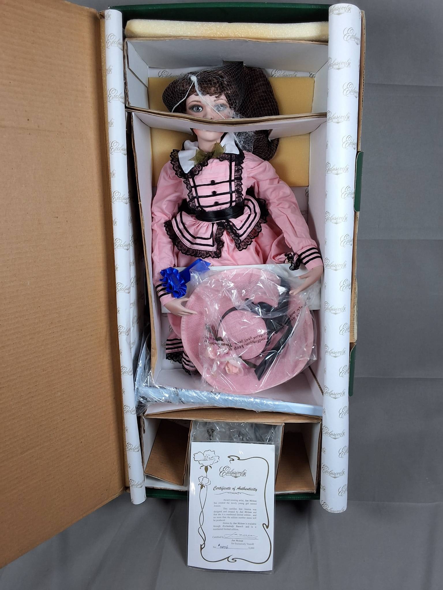 Jessica by Jan Melean: Jessica is a 24-inch doll created by Jan Melean, marked as 476 of 3000. She is dressed in a pink dress adorned with black lace trim and ribbon accents, paired with a white collar featuring delicate bo