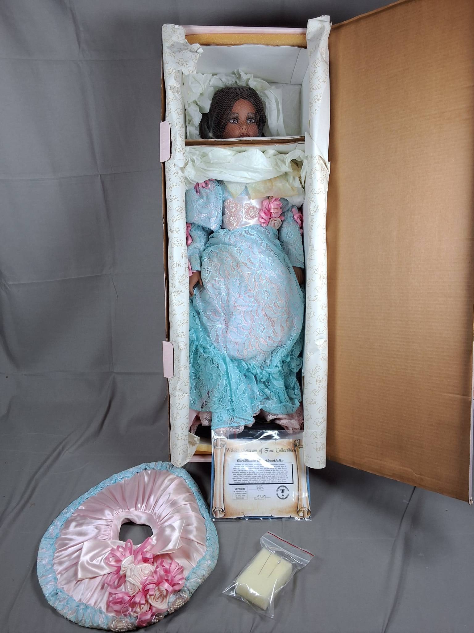 Veronica by Rustie: A 29-inch doll named Veronica, created by Rustie. This doll is number 338 of a limited run of 2000 units. Veronica is dressed in a light blue lace dress featuring floral patterns, accented by a pink s