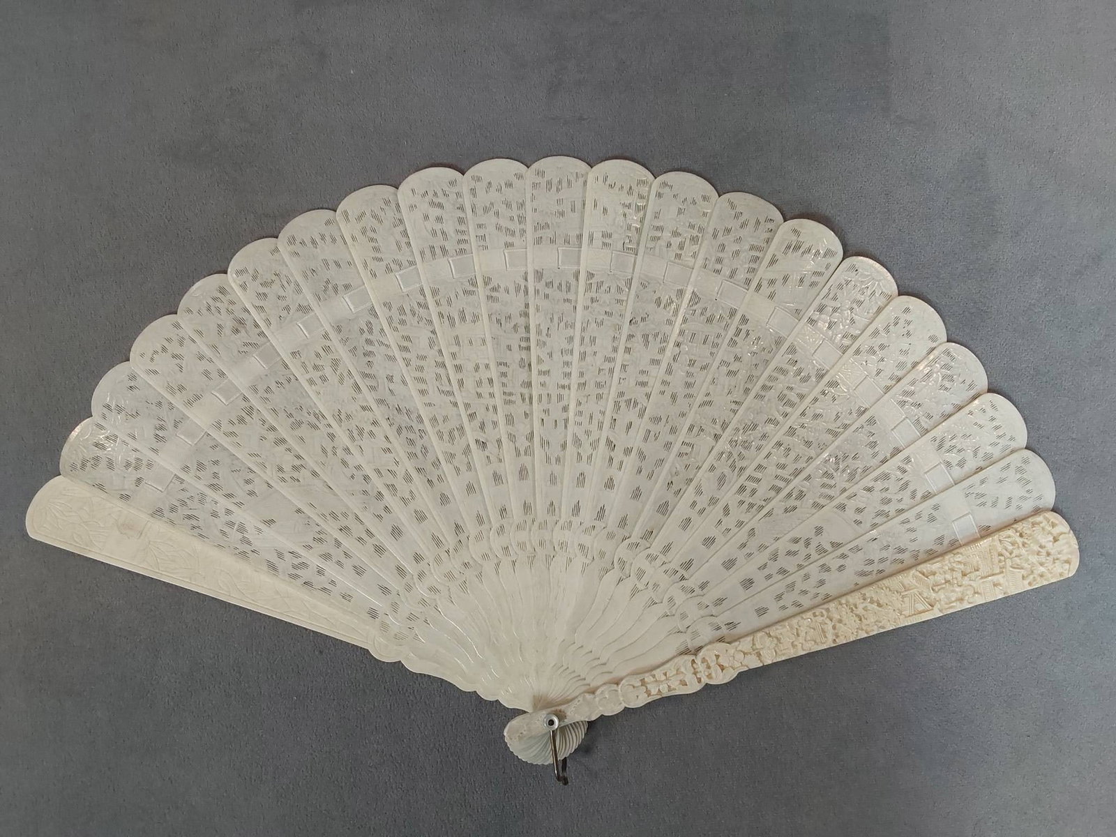 Antique Asian Carved Bone Folding Fan: Antique Asian carved bone folding fan with intricately carved guards and sticks featuring figural scenes amongst foliage. Designed in the Jenny Lind style, it is laced with a white ribbon that appears