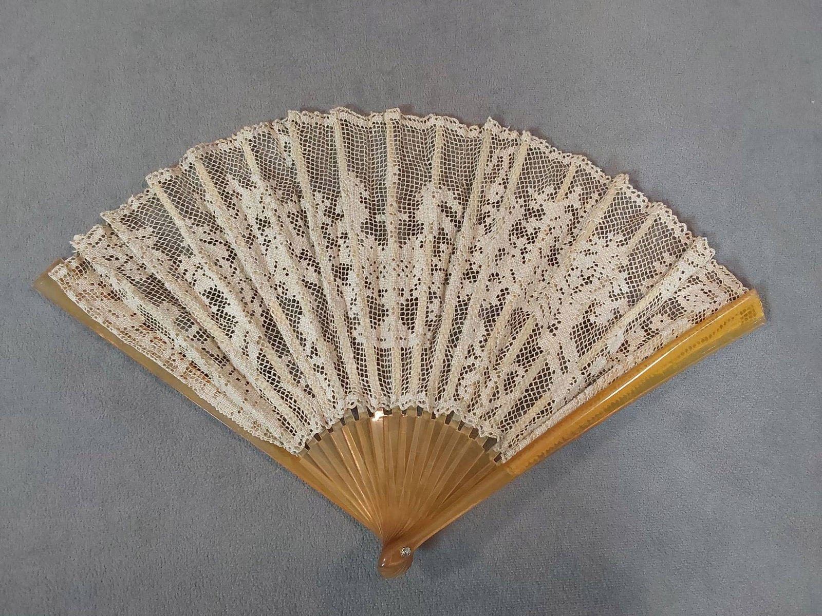Antique Filet Lace Folding Fan: Antique folding fan featuring a linen filet lace leaf in a flower and urn pattern. Guards and sticks made of horn, and painted horn upper sticks. As well as a rhinestone rivet. Dimensions measure 8 1/