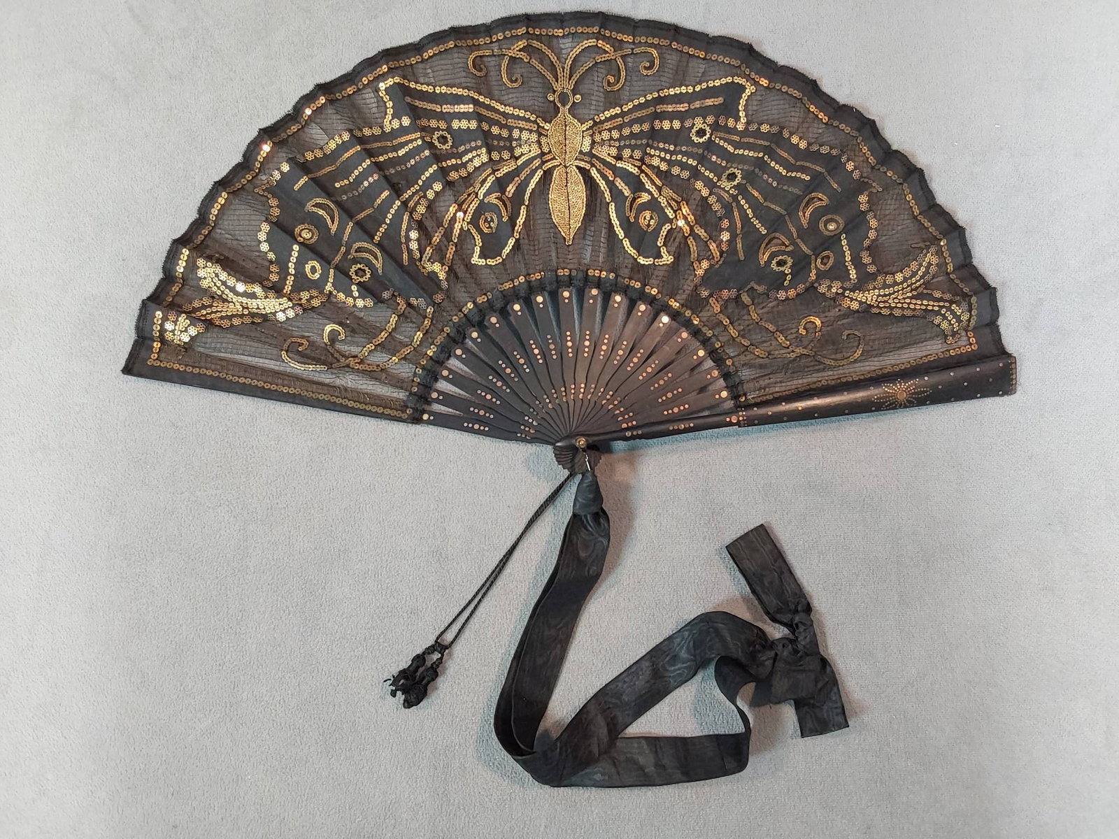 Antique Appliqued Butterfly Folding Fan - Gold Spangles: Antique folding fan adorned with a butterfly appliqued design using gold spangles, featuring painted wood guards and ribs with inlay details. The fan includes black moire ribbon, black corded wrist st