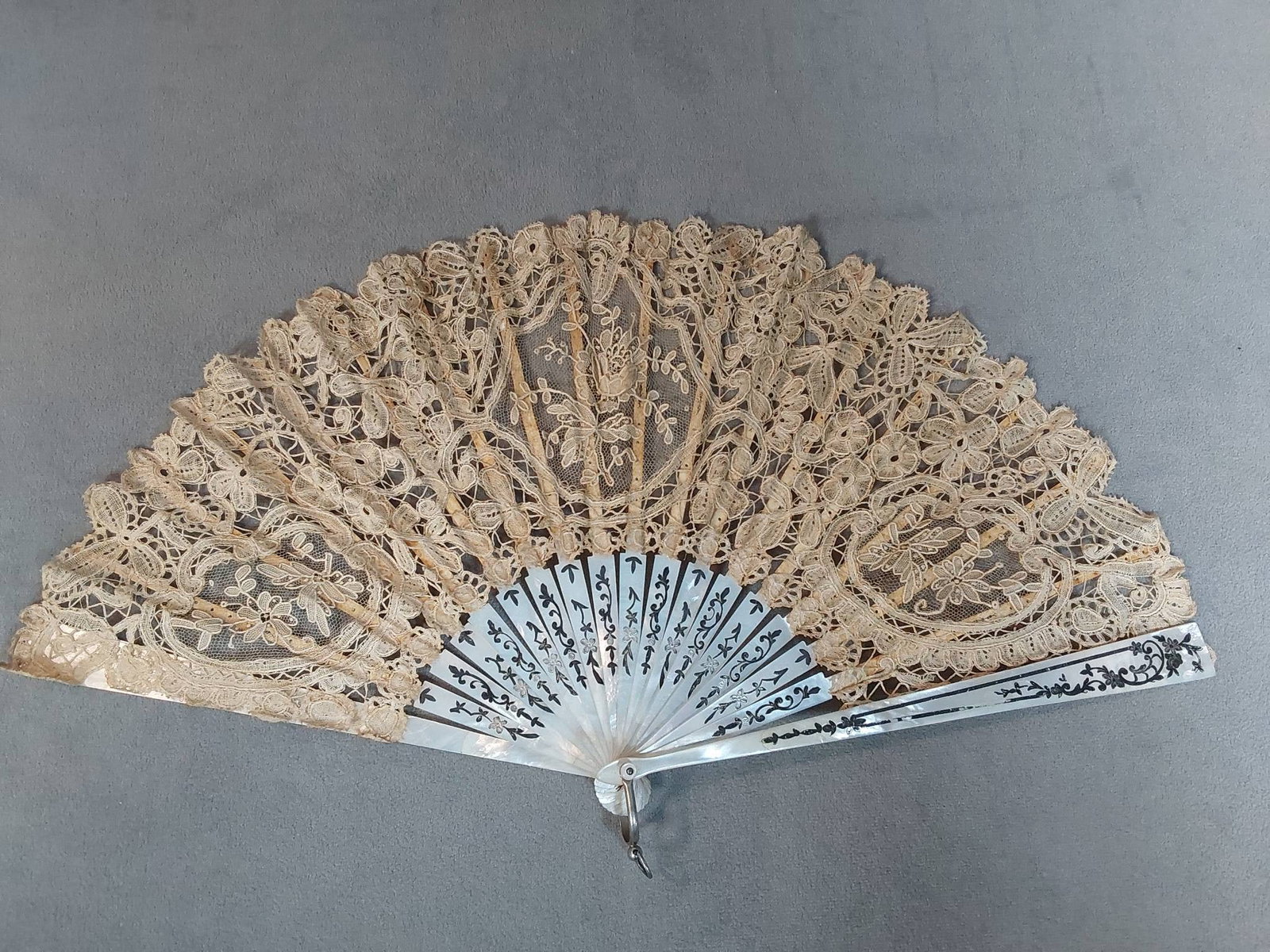 Antique Hand-Made Lace Folding Fan - Painted Wooden Box: Antique hand-made lace folding fan featuring inlay details on mother of pearl guards and ribs, with the upper section of ribs crafted from bone. The inlay on the guard exhibits wear, and there is some