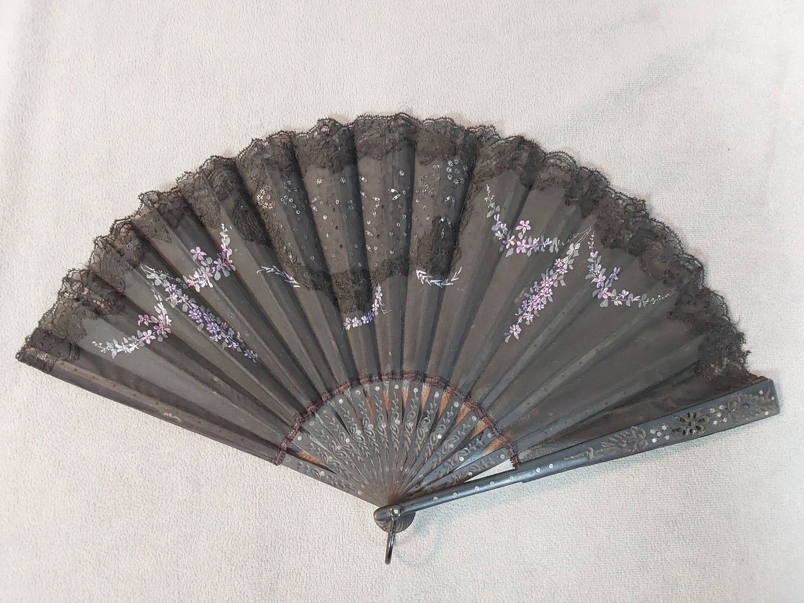 Antique Lace Applique Folding Fan - Hand Painted Floral Design: Antique lace applique folding fan featuring a hand-painted purple Forget-Me-Not floral motif. The fan is crafted with handmade lace appliqued on an organza leaf and embellished with black spangles. It