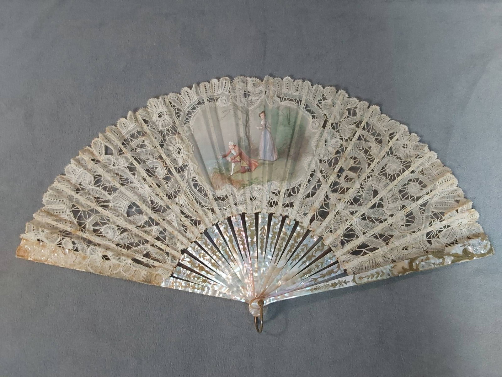 Antique Hand-Painted Folding Fan - Lace and Mother of Pearl: Antique folding fan features a handmade bobbin lace leaf, possibly of French origin. A hand-painted center medallion depicting a courtly gentleman collecting a posy of wildflowers for his lover who wa
