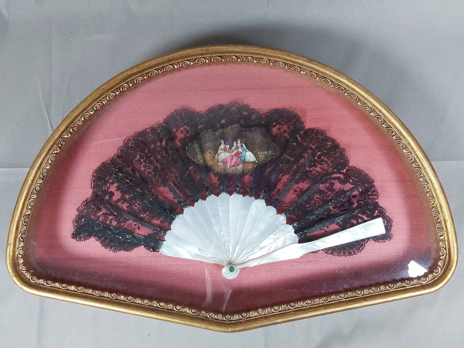 Framed Antique Lace Folding Fan - Hand-Painted Detail, Signed Mesteve: A petite framed 19th century black needle lace folding fan featuring a hand-painted center medallion with four 18th century women reclining in a pastoral setting, signed Mesteve. The guards and ribs a