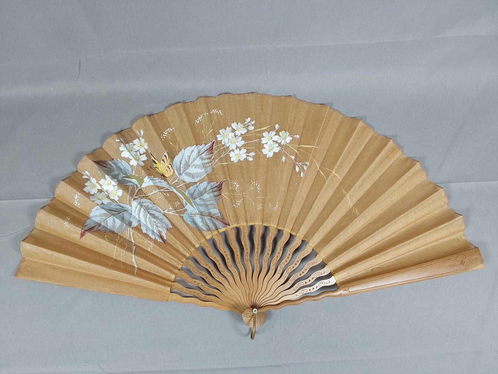 Antique Hand-Painted Silk Folding Fan - Floral and Butterfly Motif: Antique folding fan featuring a hand-painted sheer silk leaf with a hand painted floral and butterfly motif, enhanced with applied silver metallic accents. The fan is supported by carved and pierced w
