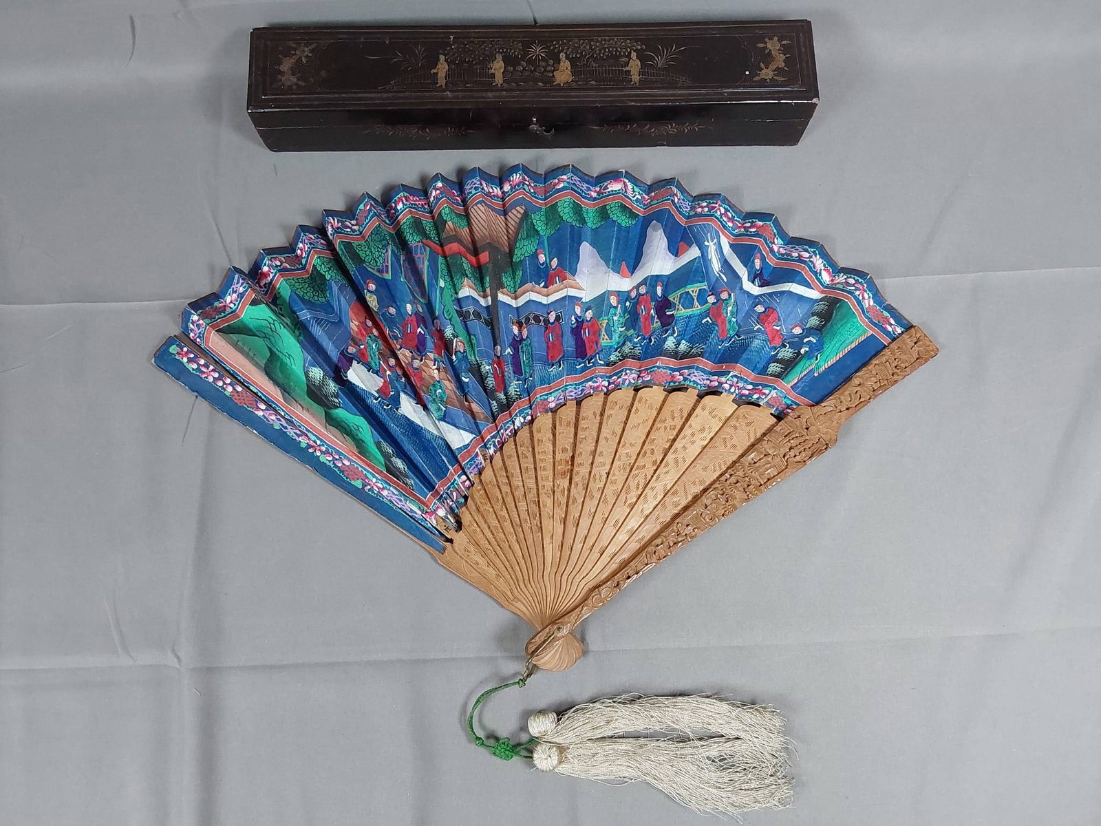 Antique Asian Hand Painted Folding Fan - Carved Wood Guards and Lacquer Box: Antique Asian paper folding fan featuring vibrant hand-painted double-sided scenes with period male figures wearing applied silk robes. The rib structure features intricately carved wooden guards and 