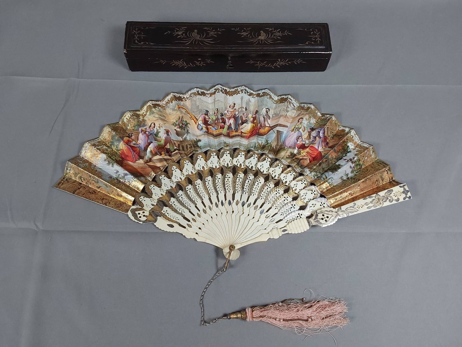 Antique Hand-Colored Folding Fan - Bone Guards and Lacquer Box: Antique paper folding fan featuring decorative gold embossed foil paper with scenes of Venetian's on gondolas and at recreation with hand painted accents on the front leaf. The reverse leaf features g