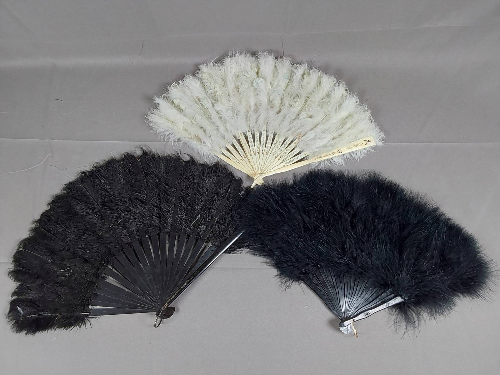 3 Antique Feather Fans: Set includes three antique feather fans: a black ostrich feather fan with wooden guards and ribs, measuring 12 1/2 in x 20 in with two detached ribs; a pale blue marabou feather fan with carved bone g