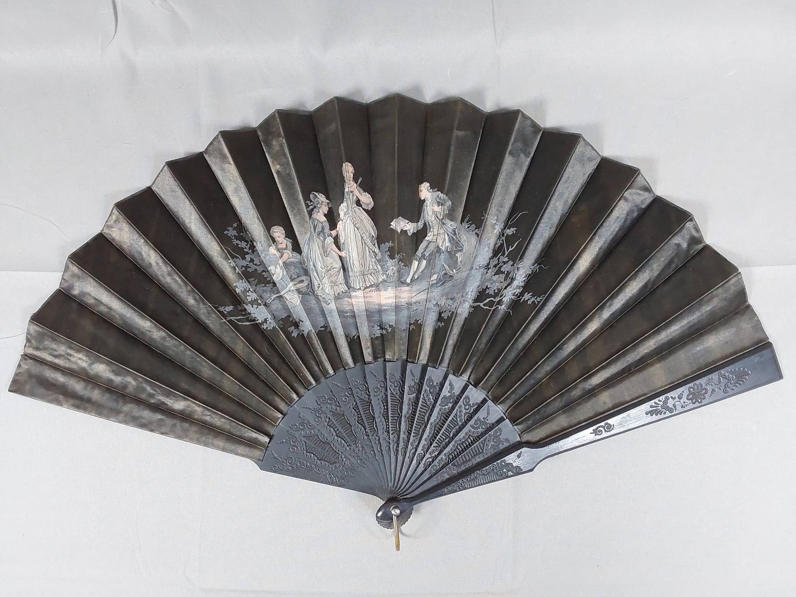 Antique Black Silk Fan - Hand Painted Figures: Antique black silk fan featuring hand-painted figures on the leaf, with carved wood guards and ribs. Accented with a metal loop and a mother of pearl rivet. The fan measures 22 1/2" x 22 1/2". Shows s