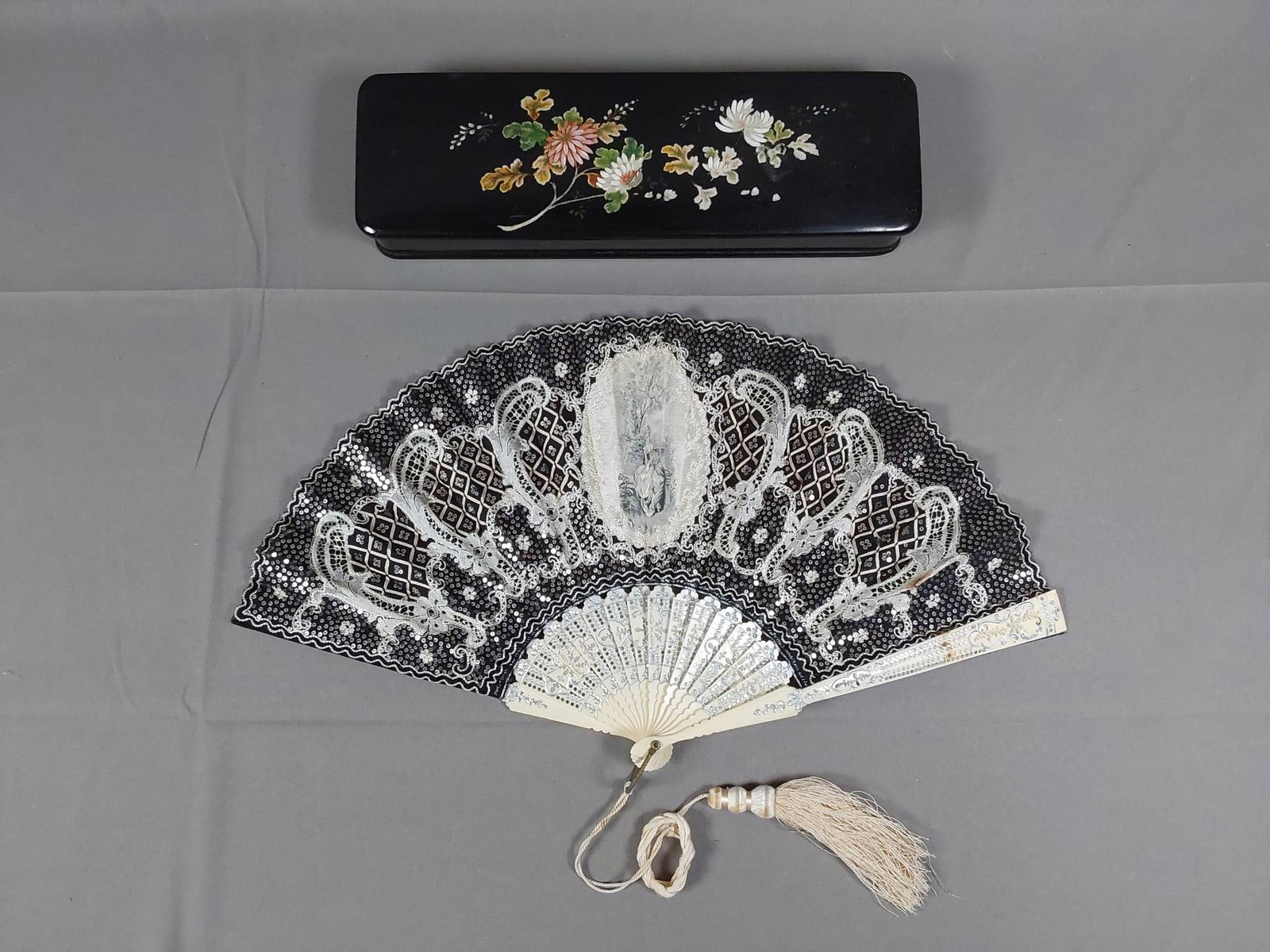 Antique Organza Folding Fan - Brocade, Lace Applique, and Silver Spangles: Antique black silk organza folding fan featuring a center silk brocade medallion of an 18th century women, lace applique, chain stitched accents, ribbon lattice accents, intricately carved guards and 