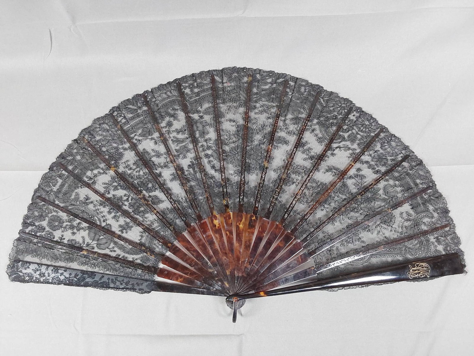 Antique Black Chantilly Lace Folding Fan - Monogram: An antique black Chantilly lace folding fan featuring tortoise shell or celluloid guards and ribs. The upper guards are intricately carved and include a possibly sterling LSJ monogram on one guard, an