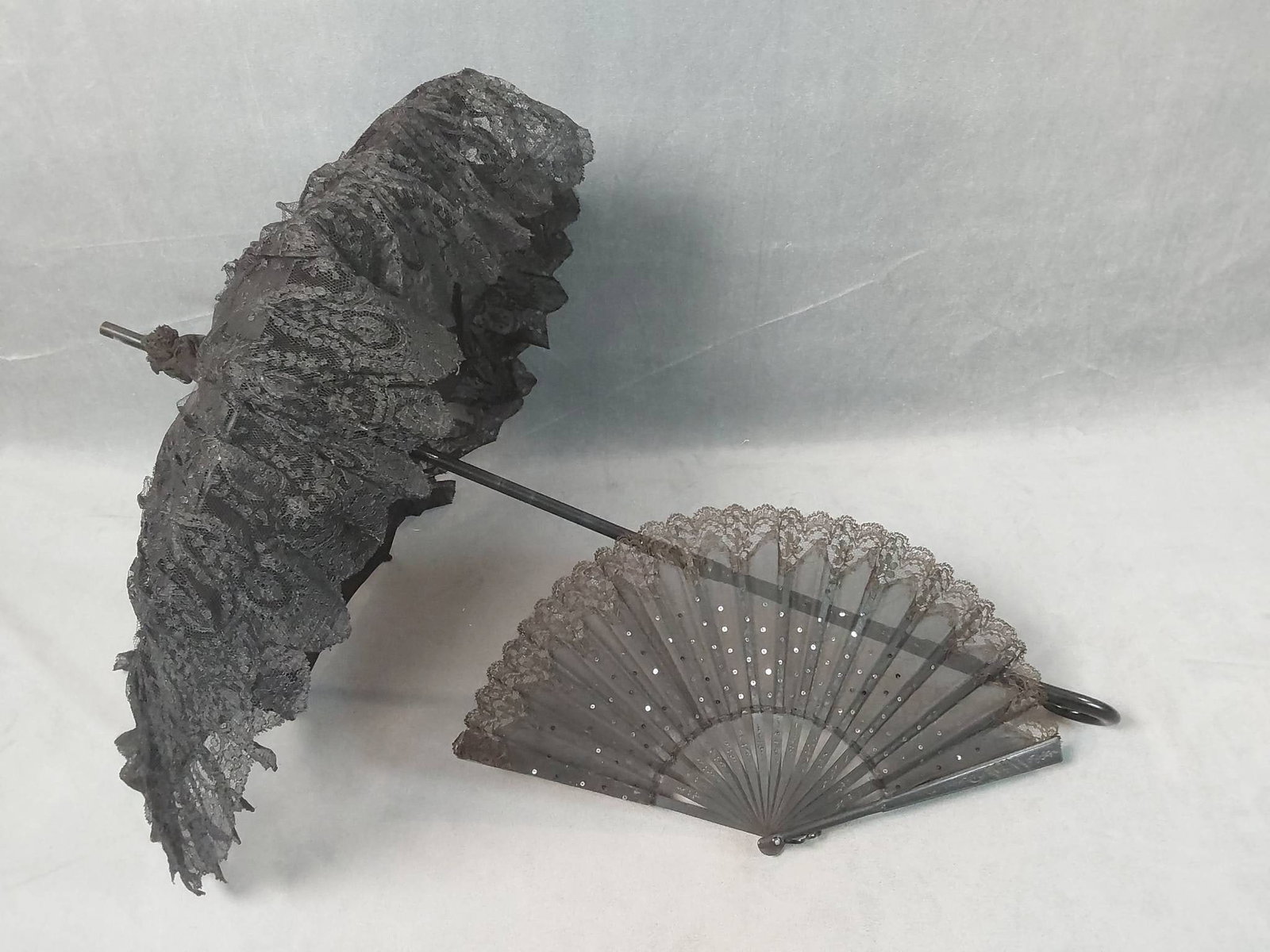 2 Victorian Mourning Accessories, Antique Black Lace Folding Parasol and Silk Fan: Lot includes two Victorian mourning accessories. The black lace folding parasol features a carved wooden hooked handle, showing some lightly soiled areas, a tear in the lace, and one rib that is no lo