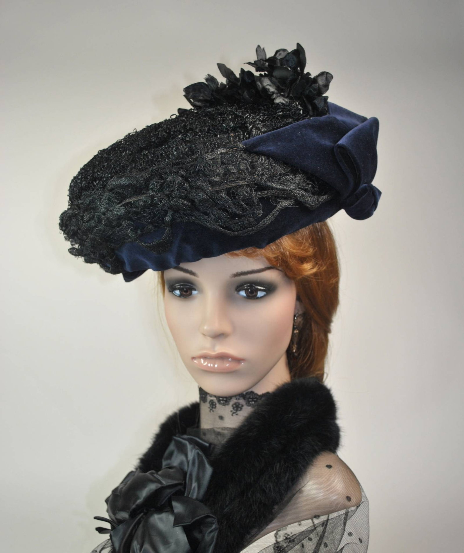 Antique Perching Hat: Antique black fine straw braid perching hat from the 1910s. The hat's design features a wire frame base with a steel blue velveteen underside and decorative bows, accentuated by black satin flowers fo