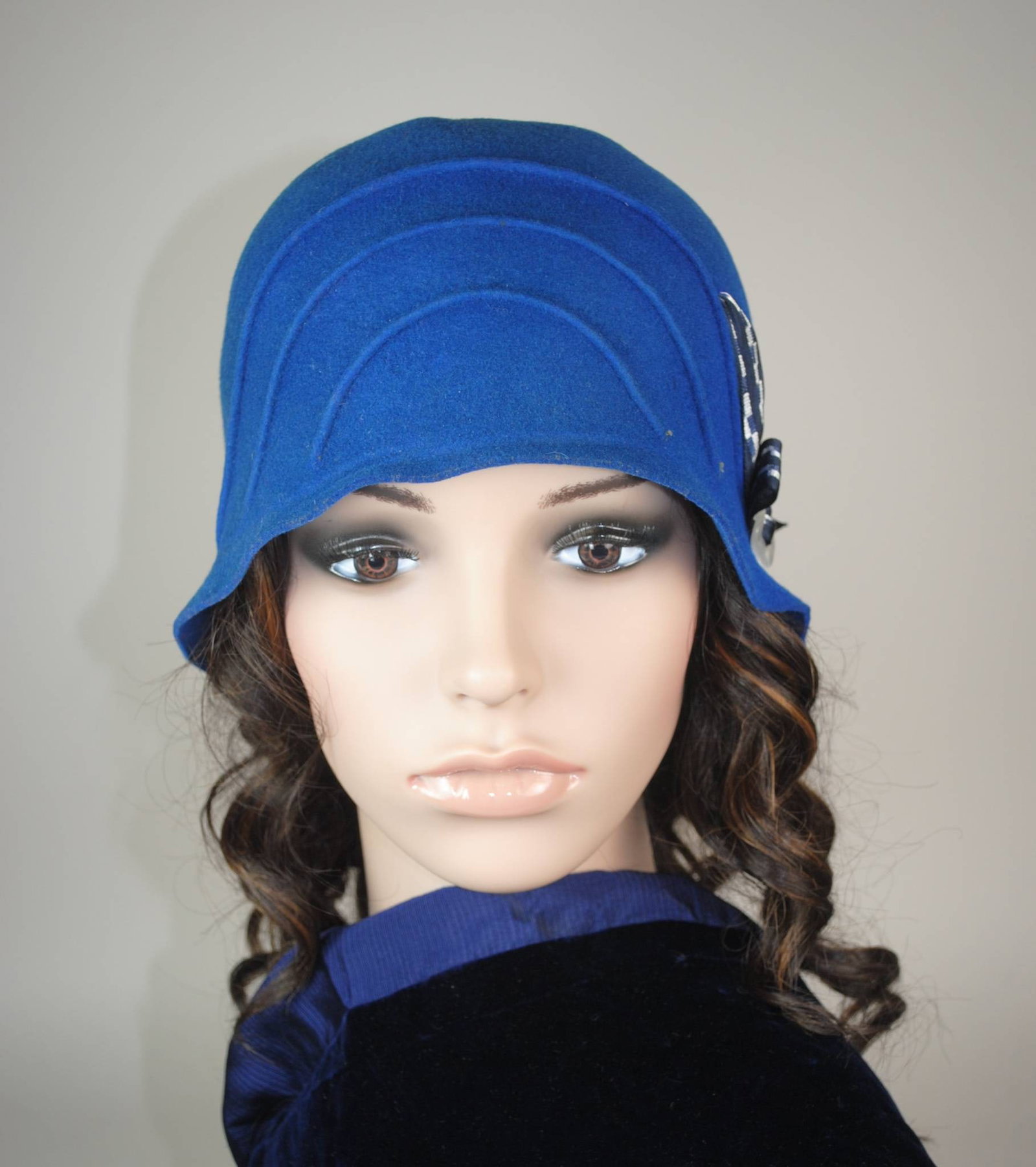 Antique Blue Felt Cloche Hat: An antique blue wool felt hat featuring three crescent-shaped stitches across the front. The hat is accented with a white pearl buckle and a navy patterned ribbon, styled in an antique cloche design. 